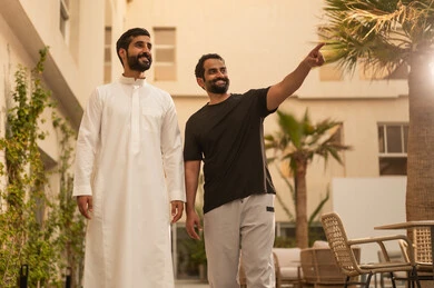 ايماءات السعادة والمتعة، أنشطة شبابية في الهواء الطلق، قضاء وقت ممتع ومسلي برفقة الاصدقاء، صديقان عربيان خليجيان سعوديان يقومان بالتجول والمشي في الحديقة