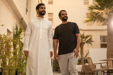 Spending enjoyable and entertaining time with friends, two Arab Gulf friends from Saudi Arabia are strolling and walking in the park, gestures of happiness and fun, youth activities in the open air.