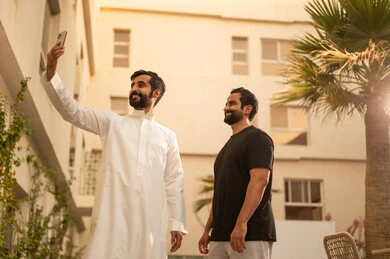 Taking a commemorative selfie using a mobile phone, gestures of happiness and enjoyment, youth activities outdoors, having a fun and entertaining time with friends, two Arab Gulf friends from Saudi Arabia are strolling and walking in the park.