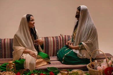 عادات الزواج والاحتفال الشعبي، تقديم هدايا الزفاف ، تعابير السعادة و السرور ، امراه عربيه خليجيه اماراتية ترتدي عباءة مطرزة تجلس مع العروس و يقومون بالمناقشة فى شي ما