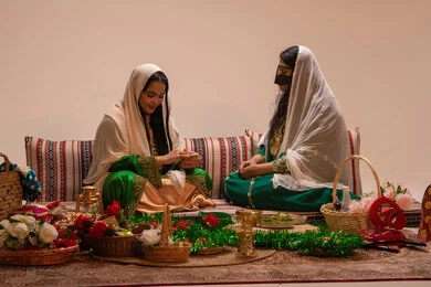 Expressions of happiness and joy, presenting wedding gifts, an Emirati Gulf Arab woman wearing an embroidered abaya sitting with the bride and discussing something, marriage customs and popular celebrations.