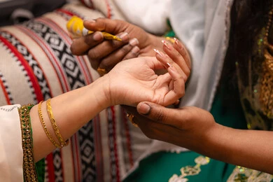 التجمل بالمظهر الشعبي الأصيل، مظاهر الاحتفال بالأعراس على النهج التراثي، زخارف وفنون يدويه من مواد طبيعيه، صورة مقربة ليد امراة عربية خليجية إماراتية تقوم برسم و نقش الحنة على يد العروس ، مهن وأزياء تقليدية شعبية نسائية