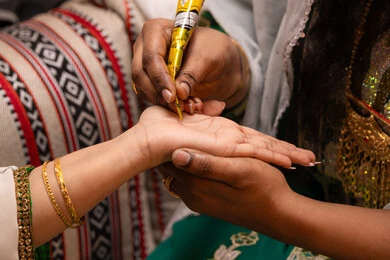 Aspects of celebrating weddings in a traditional manner, beautifying with authentic popular appearance, decorations and handicrafts made from natural materials, a close-up image of the hand of an Emirati Gulf Arab woman drawing and engraving henna on the bride's hand, traditional women's professions and attire.