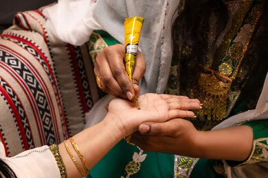 تقاليد الفرح في المناسبات الشعبية، التجمل بالمظهر الشعبي الأصيل، زخارف وفنون يدويه من مواد طبيعيه، صورة مقربة ليد امراة عربية خليجية إماراتية تقوم برسم و نقش الحنة على يد العروس ، مهن وأزياء تقليدية شعبية نسائية