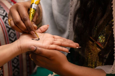 احتفالات الزواج بالعادات القديمة، التجمل بالمظهر الشعبي الأصيل، زخارف وفنون يدويه من مواد طبيعيه، صورة مقربة ليد امراة عربية خليجية إماراتية تقوم برسم و نقش الحنة على يد العروس ، مهن وأزياء تقليدية شعبية نسائية