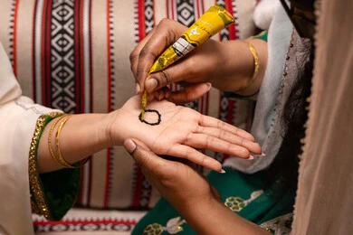 مراسم الزواج والاحتفالات التراثية، التجمل بالمظهر الشعبي الأصيل، زخارف وفنون يدويه من مواد طبيعيه، صورة مقربة ليد إمرأة عربية خليجية إماراتية تقوم برسم و نقش الحنة على يد العروس ، مهن وأزياء تقليدية شعبية نسائية