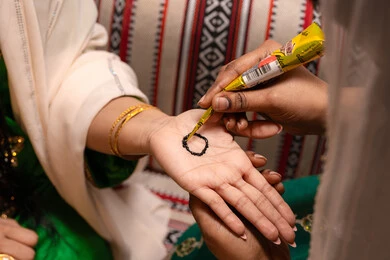 طقوس وعادات اماراتية في المناسبات السعيدة، التجمل بالمظهر الشعبي الأصيل، زخارف وفنون يدويه من مواد طبيعيه، صورة مقربة ليد إمرأة عربية خليجية إماراتية تقوم برسم و نقش الحنة على يد العروس ، مهن وأزياء تقليدية شعبية نسائية