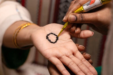 تقاليد خليجية اماراتية في الأعراس والمناسبات، التجمل بالمظهر الشعبي الأصيل، زخارف وفنون يدويه من مواد طبيعيه، صورة مقربة ليد إمرأة عربية خليجية إماراتية تقوم برسم و نقش الحنة على يد العروس ، مهن وأزياء تقليدية شعبية نسائية