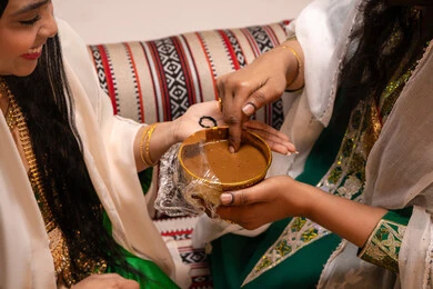 احتفالات وأفراح بطابع تراثي، التجمل بالمظهر الشعبي الأصيل، زخارف وفنون يدويه من مواد طبيعيه، صورة مقربة ليد إمرأة عربية خليجية إماراتية تقوم برسم و نقش الحنة على يد العروس ، مهن وأزياء تقليدية شعبية نسائية