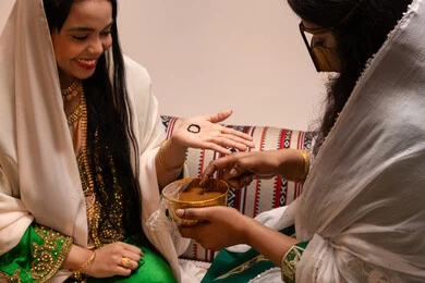 تقاليد وعادات في المناسبات السعيدة، التجمل بالمظهر الشعبي الأصيل، زخارف وفنون يدويه من مواد طبيعيه، صورة مقربة ليد إمرأة عربية خليجية إماراتية تقوم برسم و نقش الحنة على يد العروس ، مهن وأزياء تقليدية شعبية نسائية