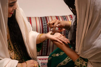 الأشغال اليدوية التراثية الدقيقة، مهن وأزياء تقليدية شعبية نسائية، مظاهر الفرح والسرور في الأعراس، تقاليد الزواج والاحتفال الخليجي، الاستعداد للمناسبات السعيدة، تصوير مقرب ليد إمرأة عربية خليجية إماراتية تقوم برسم و نقش الحنة على يد العروس