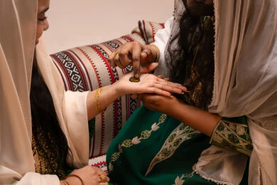 فنون يدوية مصنوعة من مواد طبيعية، مهن وأزياء تقليدية شعبية نسائية، مظاهر الفرح والسرور في الأعراس، تقاليد الزواج والاحتفال الخليجي، الاستعداد للمناسبات السعيدة، تصوير مقرب ليد إمرأة عربية خليجية إماراتية تقوم برسم و نقش الحنة على يد العروس