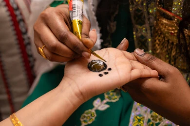Handicrafts and arts made from natural materials, expressions of joy and happiness in weddings, marriage traditions and Gulf celebrations, preparations for happy occasions, a close-up shot of the hand of an Emirati Gulf Arab woman drawing and decorating henna on the bride's hand, traditional women's professions and attire.