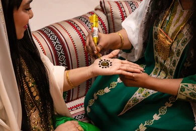 التجهيز لحفلات الزفاف، تقاليد الزواج والاحتفال الخليجي، الاستعداد للمناسبات السعيدة، زخارف وفنون يدويه من مواد طبيعيه، تصوير مقرب ليد إمرأة عربية خليجية إماراتية تقوم برسم و نقش الحنة على يد العروس ، مهن وأزياء تقليدية شعبية نسائية