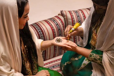 الزينة والتجمل في الأعراس، تقاليد الزواج والاحتفال الخليجي، الاستعداد للمناسبات السعيدة، زخارف وفنون يدويه من مواد طبيعيه، تصوير مقرب ليد إمرأة عربية خليجية إماراتية تقوم برسم و نقش الحنة على يد العروس ، مهن وأزياء تقليدية شعبية نسائية