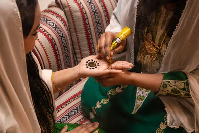 تقاليد الزواج والاحتفال الخليجي، الاستعداد للمناسبات السعيدة، زخارف وفنون يدويه من مواد طبيعيه، تصوير مقرب ليد إمرأة عربية خليجية إماراتية تقوم برسم و نقش الحنة على يد العروس ، مهن وأزياء تقليدية شعبية نسائية