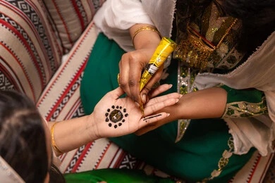 التجمل بلمسات من الأصالة الشعبية، زخارف وفنون يدويه من مواد طبيعيه، عادات وتقاليد في المناسبات والأفراح السعيدة، تصوير مقرب ليد إمرأة عربية خليجية إماراتية تقوم برسم و نقش الحنة على يد العروس ، مهن وأزياء تقليدية شعبية نسائية