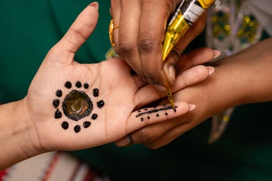 Care for beauty in the traditional way, decorations and handicrafts made from natural materials, customs and traditions in happy occasions and celebrations, close-up photography of the hand of an Arab Gulf Emirati woman drawing and engraving henna on the bride's hand, traditional women's professions and attire.