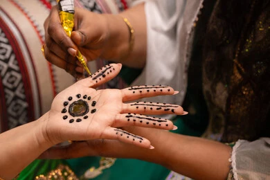 Embellishing with the authentic popular appearance, decorations and handicrafts made from natural materials, customs and traditions in happy occasions and celebrations, a close-up shot of the hand of an Emirati Gulf Arab woman drawing and engraving henna on the bride's hand, traditional women's professions and attire.