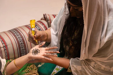 Interest in beauty in a traditional style, decorations and handicrafts made from natural materials, customs and traditions in happy occasions and celebrations, a close-up shot of the hand of an Emirati Gulf Arab woman drawing and engraving henna on the bride's hand, traditional women's professions and attire.
