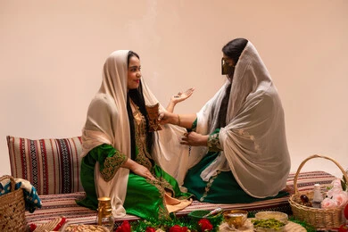 عطور عربية من المسك والعود، أصالة العادات والتقاليد الخليجية، الاحتفال بالمناسبات والأفراح السعيدة, امراة عربية خليجية اماراتية ترتدي الزي الشعبي تحمل بيدها حامل البخور( المبخرة ) تقوم بتبخير العروس، مراسم الأعراس والزواج