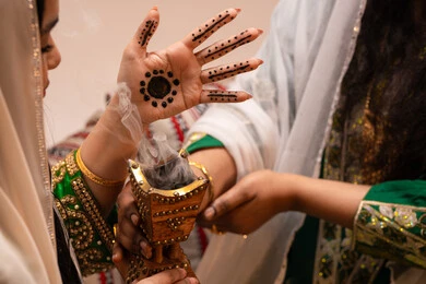 استخدام المسك والعود، أصالة العادات والتقاليد الخليجية، الاحتفال بالمناسبات والأفراح السعيدة, امراة عربية خليجية اماراتية ترتدي الزي الشعبي تحمل بيدها حامل البخور( المبخرة ) تقوم بتبخير العروس، مراسم الأعراس والزواج