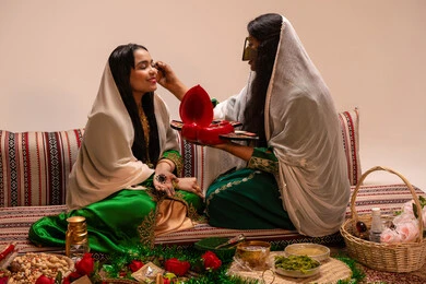 العناية بالجمال والإطلالة، ايماءات السعادة والفرح، مفهوم التزين والاطلالة المتألقة، الاحتفال بليلة العمر، منتجات ومساحيق التجميل, مناسبات وأفراح واحتفالات سعيدة، سيدة عربية خليجية اماراتية تقوم بوضع المكياج للعروسة، ارتداء الازياء التقليدية