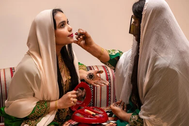 مستحضرات مكياج وألوان تجميلية، العناية والاهتمام بالأناقة والجمال، مفهوم التزين والاطلالة المتألقة، سيدة عربية خليجية اماراتية تقوم بوضع أحمر الشفاه للعروسة، إيماءات السعادة والفرح ، الاحتفال بليلة العمر