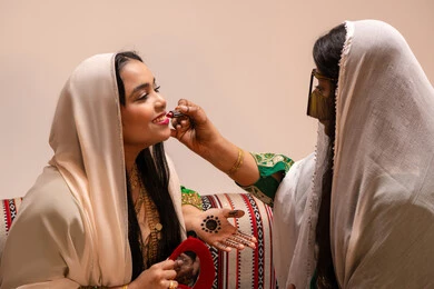 أدوات ومساحيق تجميل، العناية والاهتمام بالأناقة والجمال، مفهوم التزين والاطلالة المتألقة، سيدة عربية خليجية اماراتية تقوم بوضع أحمر الشفاه للعروسة، إيماءات السعادة والفرح ، الاحتفال بليلة العمر