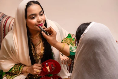 الاحتفال بليلة العمر، منتجات ومساحيق التجميل, مناسبات وأفراح واحتفالات سعيدة، العناية والاهتمام بالأناقة والجمال، مفهوم التزين والاطلالة المتألقة، سيدة عربية خليجية اماراتية تقوم بوضع أحمر الشفاه للعروسة، إيماءات السعادة والفرح