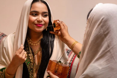 روائح عطرية فريدة ، الفرح و السرور في يوم الزواج، مفهوم الأناقة والاهتمام بالمظهر الخارجي، سيدة عربية اماراتية خليجية ترتدي البرقع وحجاب ابيض تحمل زجاجة عطرية تقوم بوضع العطر لعروس ترتدي الزي التراثي، مراسم الأعراس والاحتفالات في الامارات