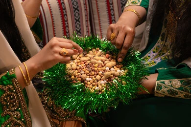 تراثيات وشعبيات اماراتيه تقليديه، ارتداء الازياء الشعبية في المناسبات والاحتفالات، منتج محلي وطني  ، صورة مقربة لامرأتان عربيتان خليجيتان اماراتيتان ترتديان الزي التقليدي تقومان بتناول المكسرات المشكلة، سناك صحي وخفيف