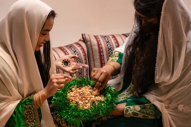 سناك صحي وخفيف، تراثيات وشعبيات اماراتيه تقليديه، ارتداء الازياء الشعبية في المناسبات والاحتفالات، منتج محلي وطني  ، صورة مقربة لامرأتان عربيتان خليجيتان اماراتيتان ترتديان الزي التقليدي تقومان بتناول المكسرات المشكلة