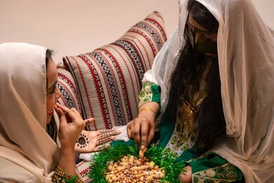 منتج محلي وطني ، ارتداء الازياء الشعبية في المناسبات والاحتفالات، تراثيات وشعبيات اماراتيه تقليديه ، امرأتان عربيتان خليجيتان اماراتيتان ترتديان الزي التقليدي تقومان بتناول المكسرات المشكلة، سناك صحي وخفيف