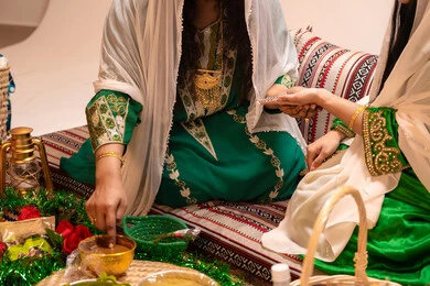 مهن وأزياء تقليدية شعبية نسائية، عادات وتقاليد في المناسبات والأفراح السعيدة، زخارف وفنون يدويه من مواد طبيعيه، التجمل والاهتمام بالمظهر الخارجي على الطريقة الشعبية، صورة مقرب لإمرأة عربية خليجية إماراتية ترتدي الزي التراثي و تقوم برسم و نقش الحنة على يد العروسة