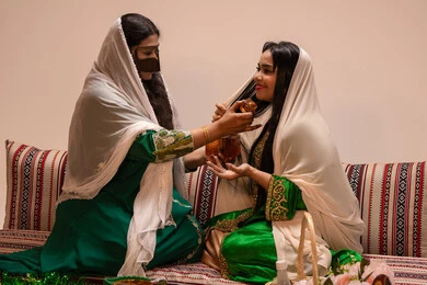 عطور فاخرة ومميزة ، الفرح و السرورفي يوم الزواج، مفهوم الأناقة والاهتمام بالمظهر الخارجي، سيدة عربية اماراتية خليجية ترتدي البرقع وحجاب ابيض تحمل زجاجة عطرية تقوم بوضع العطر لعروس ترتدي الزي التراثي، مراسم الأعراس والاحتفالات في الامارات