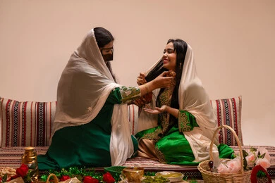 Perfumes with luxurious and unique scents, the concept of elegance and attention to appearance, an Emirati Gulf Arab woman wearing a burqa and a white hijab holding a perfume bottle applying fragrance to a bride dressed in traditional attire, wedding ceremonies and celebrations in the UAE, joy and happiness on the wedding day.