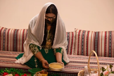 مراسم الزواج الإماراتي الشعبي، نقوش وزخارف تراثية من مواد طبيعيه، مهنة تقليدية شعبية نسائية، التجمل والتزيين في يوم الزفاف، إمرأة عربية خليجية إماراتية ترتدي البرقع وحجاب ابيض تقوم بتحضير خلطة الحناء