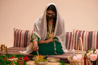 تقاليد الأعراس الإماراتية الأصيلة ، نقوش وزخارف تراثية من مواد طبيعيه، مهنة تقليدية شعبية نسائية، التجمل والتزيين في يوم الزفاف، إمرأة عربية خليجية إماراتية ترتدي البرقع وحجاب ابيض تقوم بتحضير خلطة الحناء