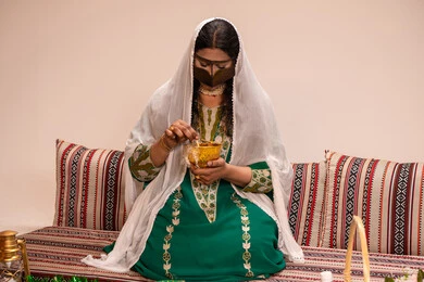 Emirati social customs, traditional engravings and decorations made from natural materials, a traditional popular women's profession, beautification and adornment on the wedding day, an Arab Gulf Emirati woman wearing a burqa and a white hijab preparing a henna mixture.