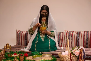 تقاليد شعبية متوارثة خلال المناسبات والأفراح ، نقوش وزخارف تراثية من مواد طبيعيه، مهنة تقليدية شعبية نسائية، التجمل والتزيين في يوم الزفاف، إمرأة عربية خليجية إماراتية ترتدي البرقع وحجاب ابيض تقوم بتحضير خلطة الحناء