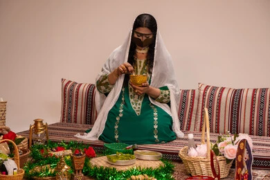 Emirati social rituals and customs, traditional engravings and decorations made from natural materials, a traditional popular women's profession, beautification and adornment on the wedding day, an Arab Gulf Emirati woman wearing a burqa and a white hijab preparing a henna mixture.