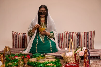 Traditional patterns and decorations made from natural materials, a traditional popular women's craft, beautification and adornment on the wedding day, customs and traditions in happy occasions and celebrations, an Arab Gulf Emirati woman wearing a burqa and a white hijab preparing a henna mixture.