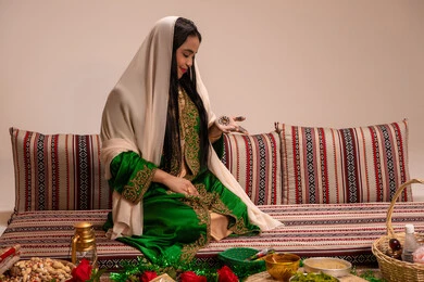 An Arab Gulf Emirati woman wearing an embroidered abaya looks at her hands with gestures of happiness and joy, the special gifts for the bride before the wedding day, arts, designs, and handmade decorations made from natural materials, customs and traditions in happy occasions and celebrations.