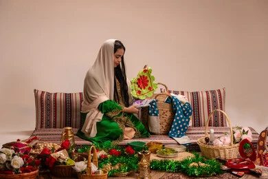 منتج محلي وطني ، تراثيات وشعبيات اماراتيه تقليديه، ارتداء الازياء الشعبية في المناسبات والاحتفالات ، امراة عربية خليجية اماراتية ترتدي العباءة المطرزة تمسك قطعة قماش مصنوعه بالتطريز اليدوي الشعبي التقليدي و تنظر اليها