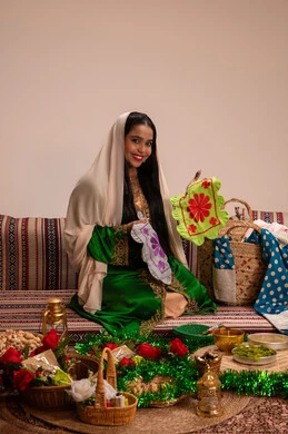 Wearing traditional folk costumes at events and celebrations, traditional Emirati heritage and folk art, a local national product, an Arab Gulf Emirati woman wearing an embroidered abaya holding a piece of fabric made with traditional hand embroidery, looking at the camera with gestures of happiness and joy.
