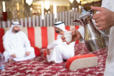 الكرم والضيافة عند العرب،إيماءات البشاشة والترحيب، صب القهوة من الدلة النحاسية، مجموعة اصدقاء عرب خليجيون اماراتيون يرتدون الكندورة والغترة يتبادلون الاحاديث، قضاء أوقات ممتعة مع الأصدقاء