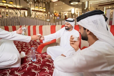 إيماءات البشاشة والترحيب، الكرم والضيافة عند العرب، صب القهوة من الدلة النحاسية، مجموعة اصدقاء عرب خليجيون اماراتيون يرتدون الكندورة والغترة يتبادلون الاحاديث، قضاء أوقات ممتعة مع الأصدقاء