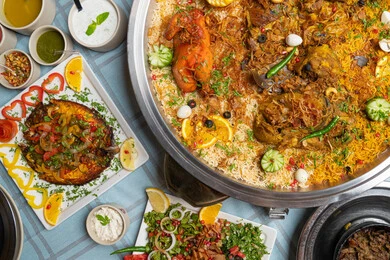 نكهات التراث العربي في الولائم والمناسبات، صورة مقربة لطبق تقليدي فاخر يحتوي على لحم الضأن المطهو بطريقة المندي، يُقدم فوق الأرز البسمتي  المتبل بالتوابل العربية الأصيلة، مزين بشرائح الليمون والبرتقال والخضار الطازجة، كرم الضيافة والمذاق الخليجي الأصيل