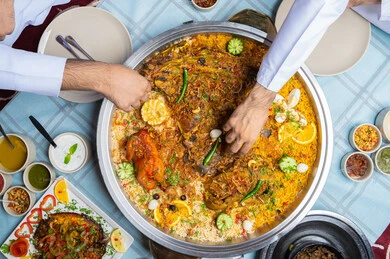 مطاعم و كافيهات الامارات, صورة مقربة ليد رجلان عربيان خليجيان إماراتيان يرتديان الكندورة والغترة، يجلسان على مائدة مليئة بالمأكولات الشرقية اللذيذة ويتشاركان الطعام,الاستمتاع بالغداء في الخارج, حسن الكرم والضيافة ,  إيماءات السعادة و السرور